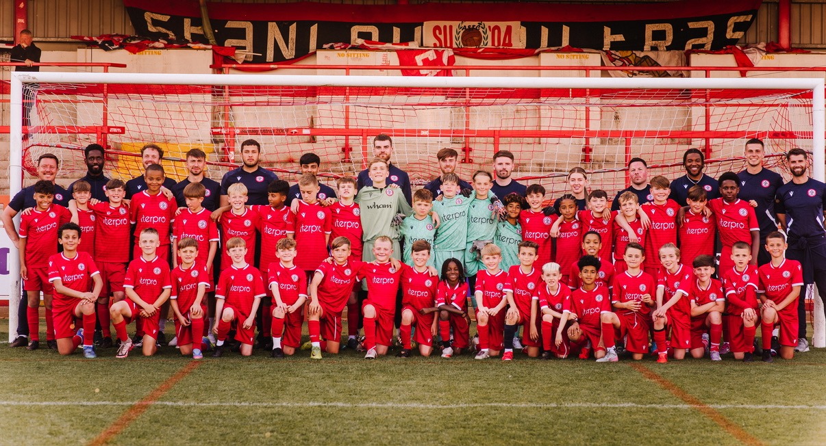 Accrington Stanley Academy Children in red Accrington Stanley kits stand in front of staff in the goalmouth