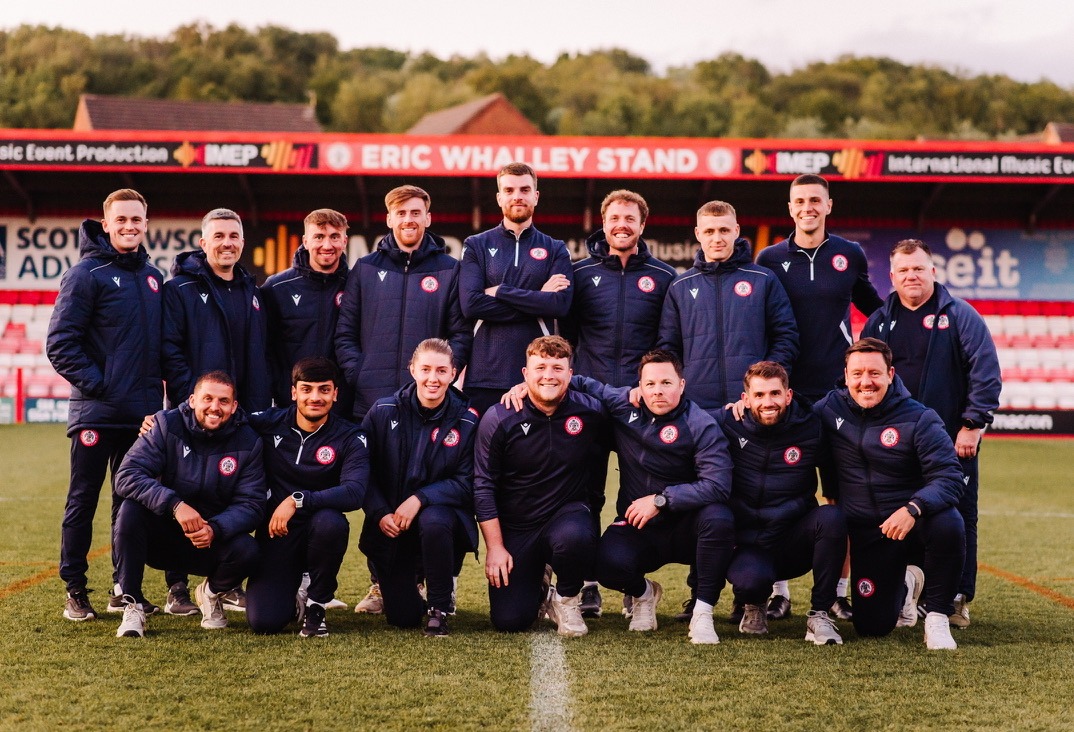 Accrington Stanley Academy Accrington Stanley Academy staff standing and kneeling in two rows on the pitch at the Wham Stadium