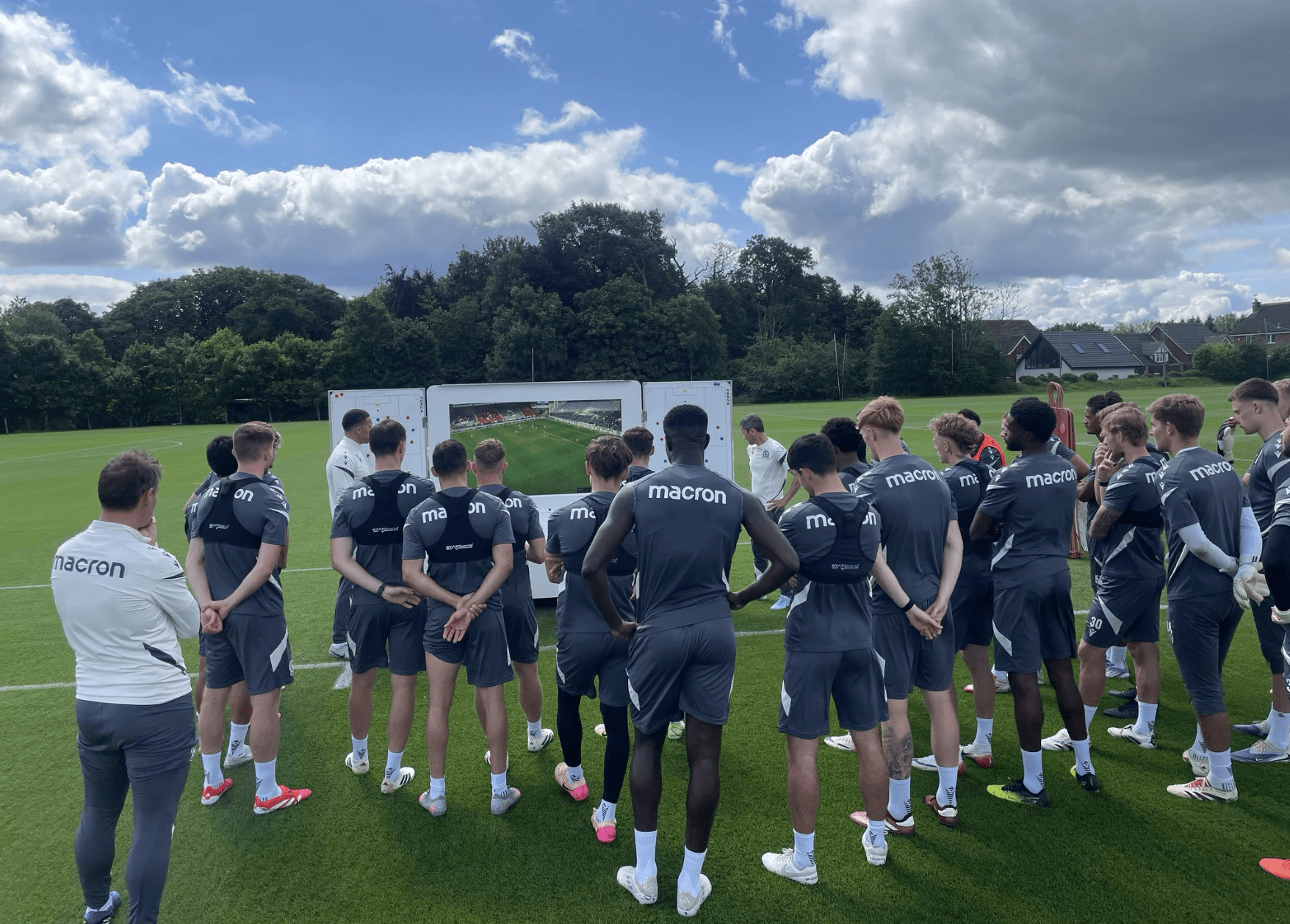 Blackburn players stand in front of a screen on a cart while staff members show them clips while on the training pitch