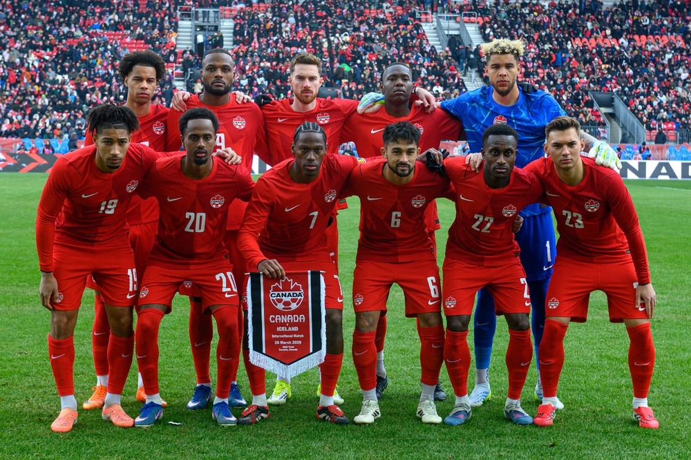 The Canada Men's National Team standing in two rows with one player holding a pennant